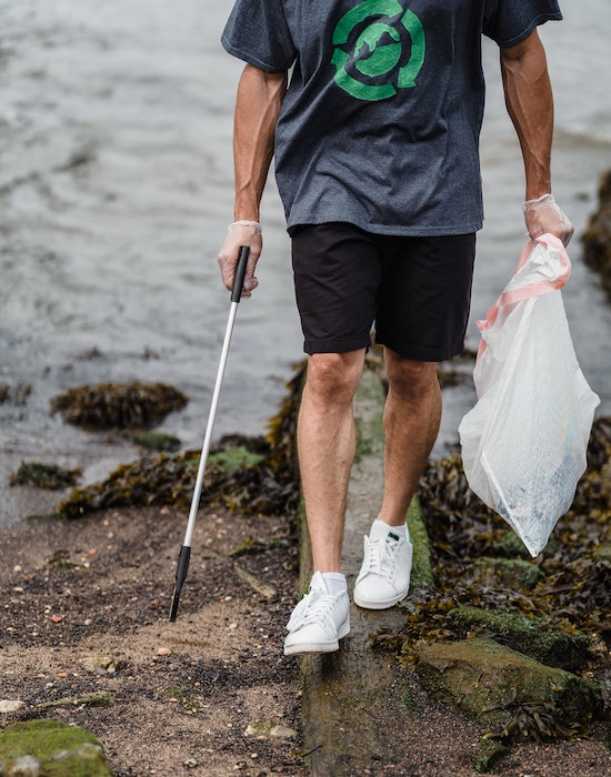 Surfer collecting trash on the beach rocks