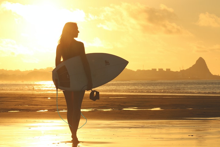 Surfer walking on the beach after surf enjoying the sunset